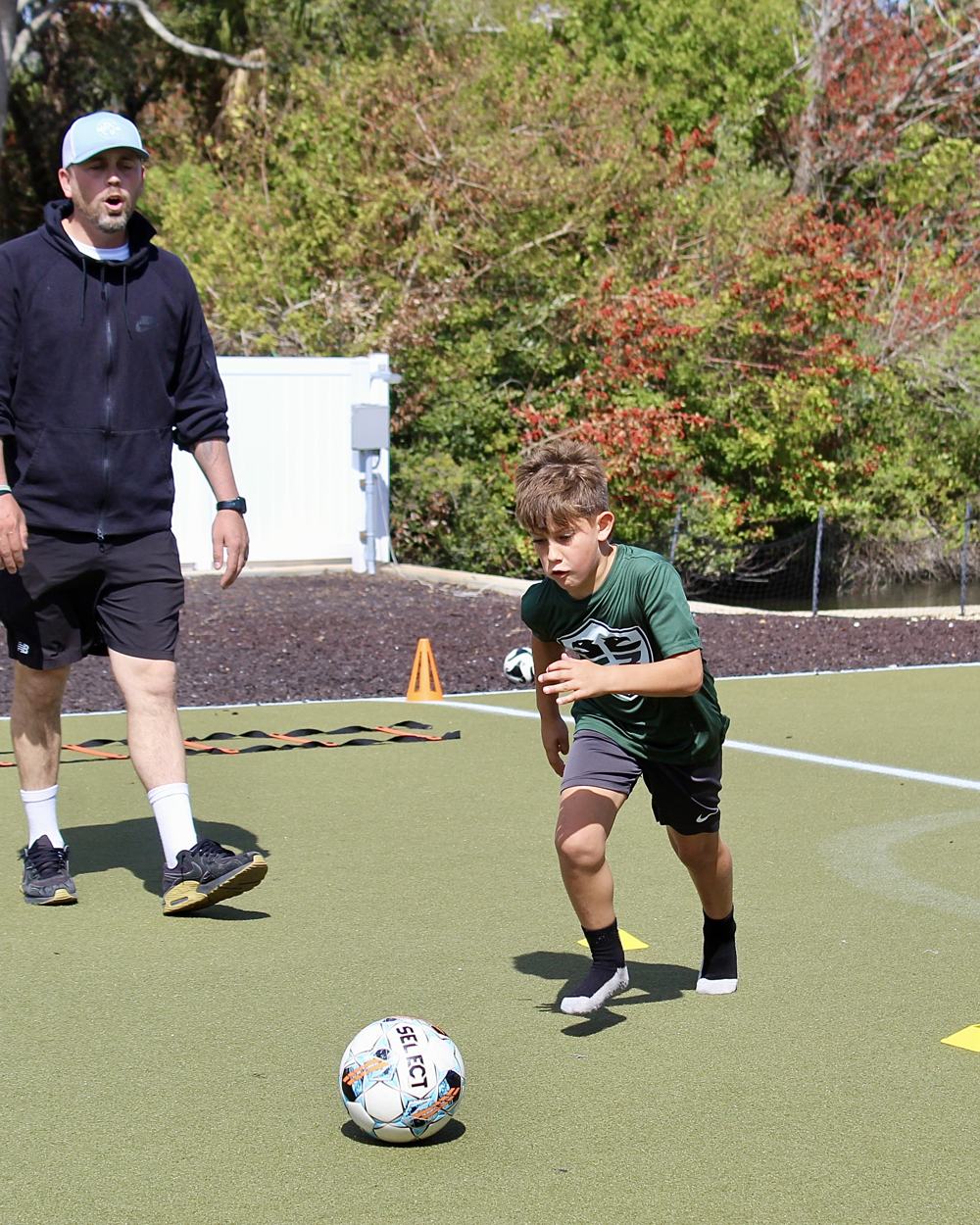 A coach watches a student dribble across the turf.