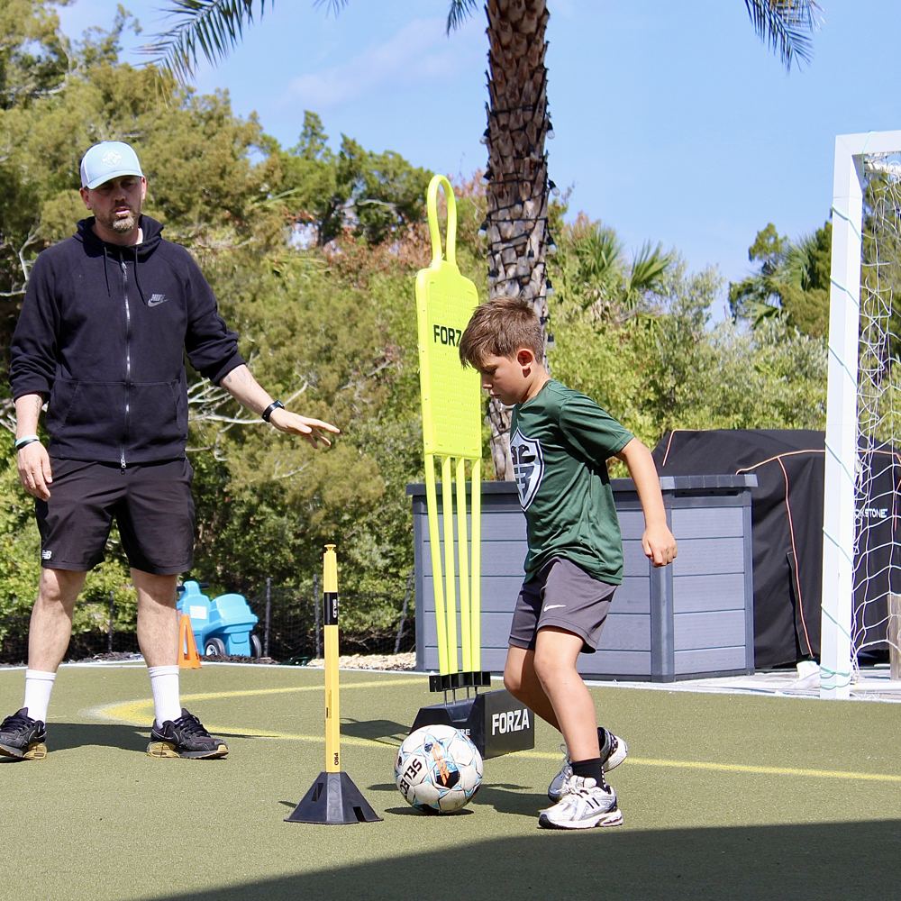 A coach guides a student dribbling past a training mannequin.