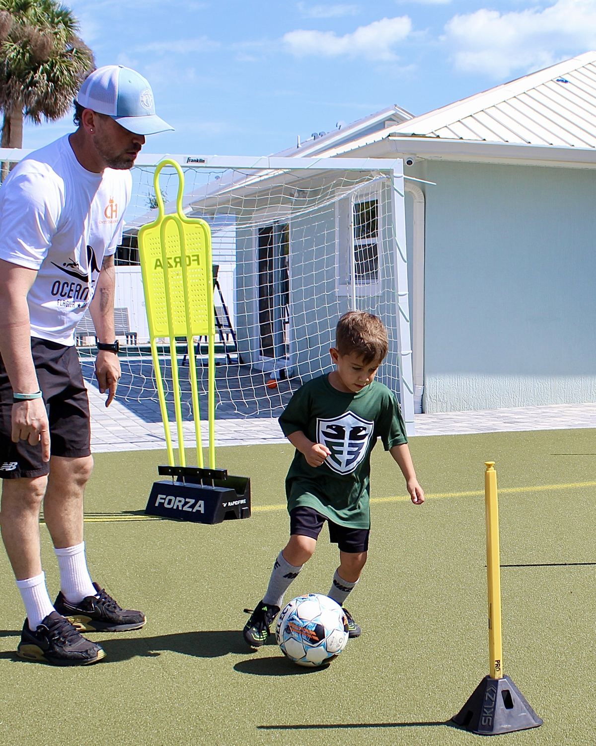A coach walks alongside a young student dribbling through a training course.