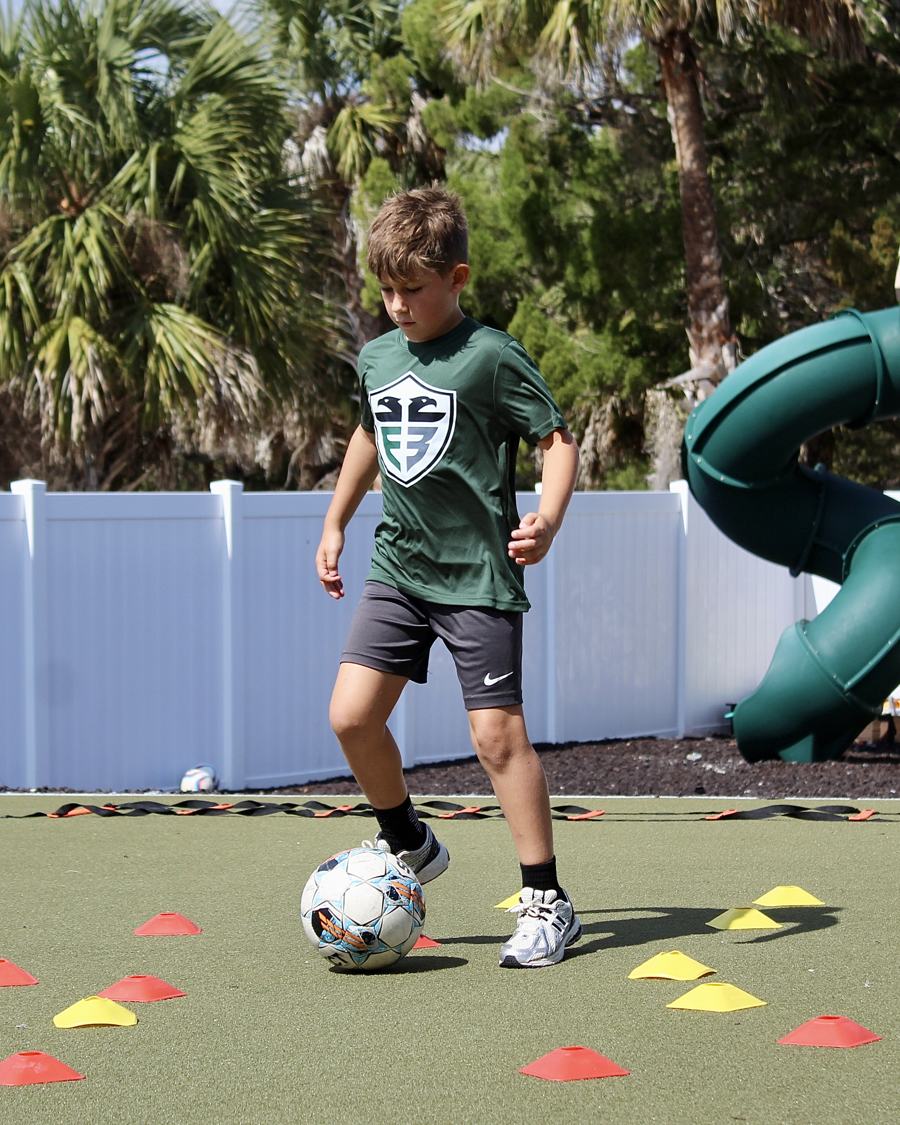 A student in a green jersey dribbles through cones.