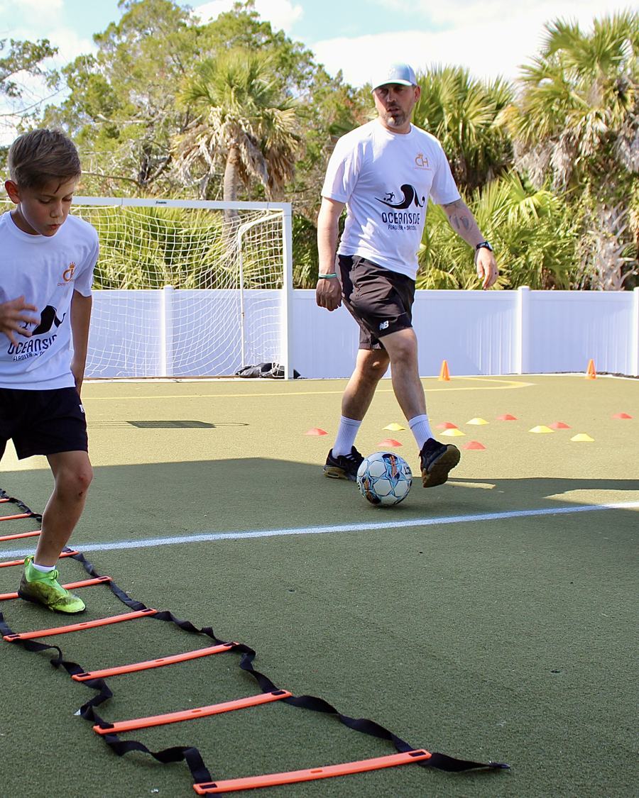 A coach runs a ball-control drill beside a footwork ladder.