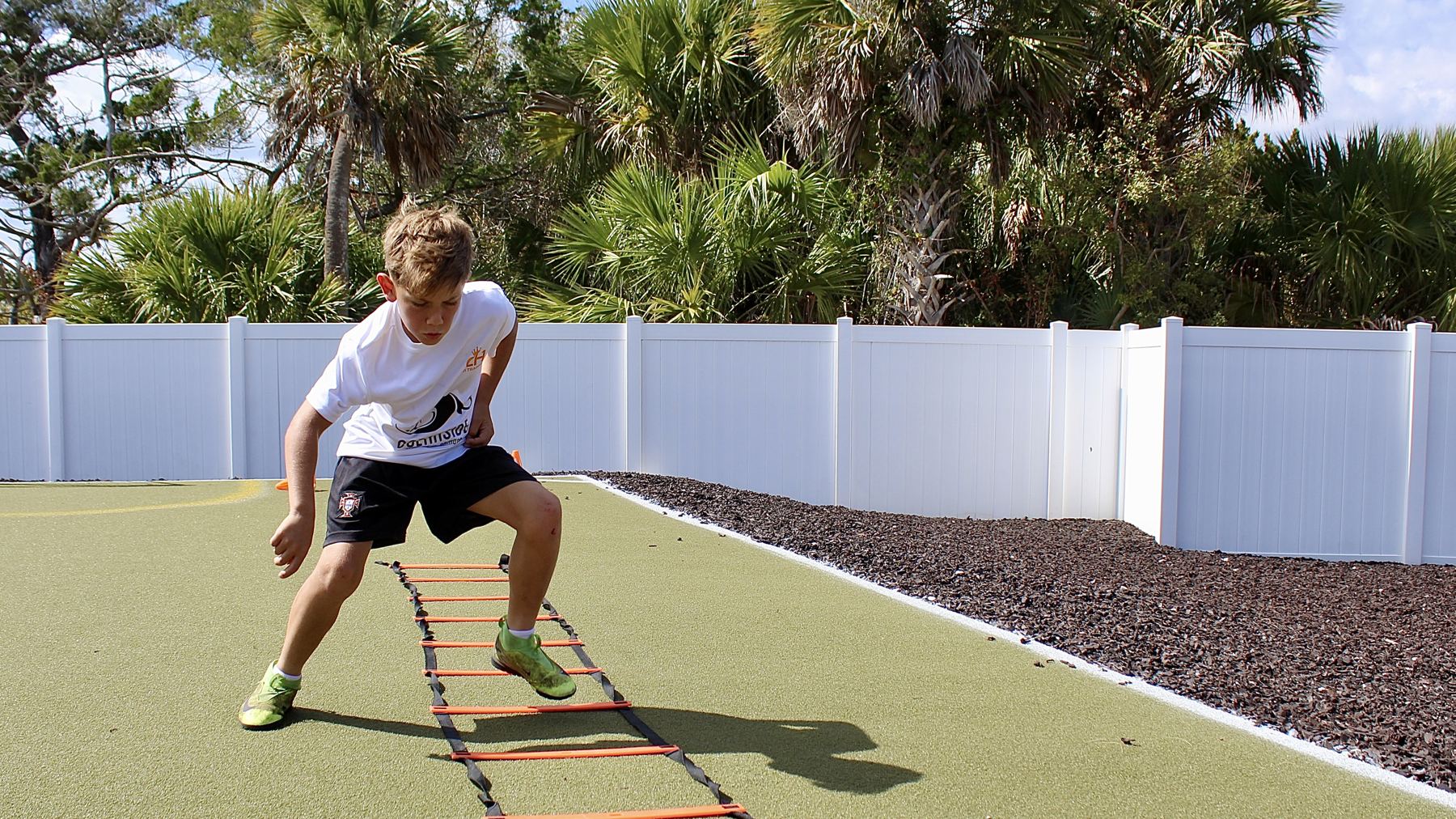 A student works through a footwork ladder drill on the academy's turf field.