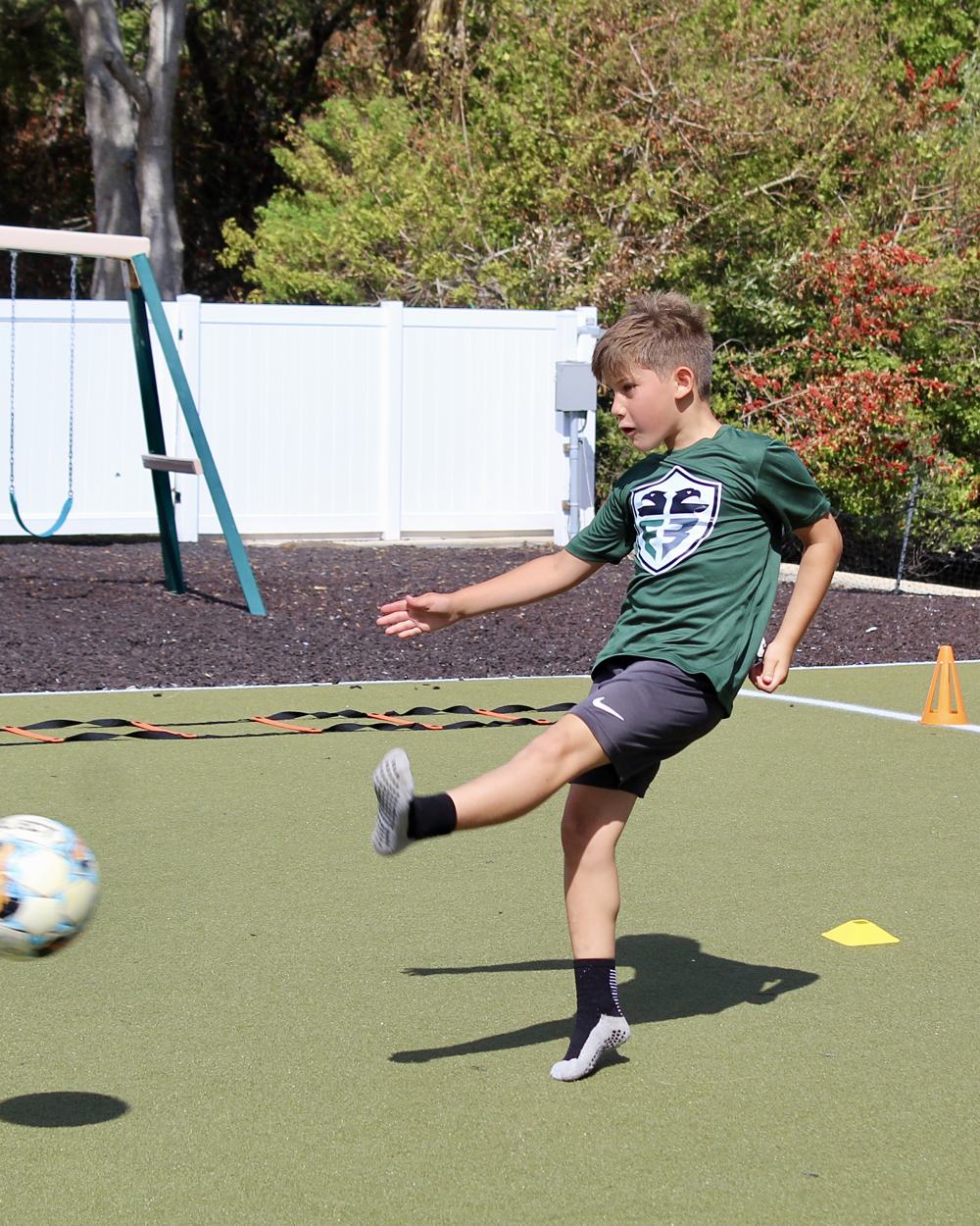 A student in a green Faith & Freedom jersey strikes the ball on the turf.